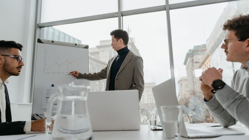 Professionals engaged in a collaborative business meeting with charts and laptops in a modern office setting. — Protect Minor
