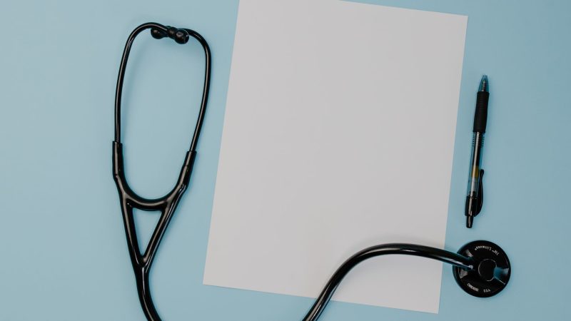Flat lay of a stethoscope, blank paper, and pen on a blue background. — Stuart Piltch New York: Building Confidence in Wellne