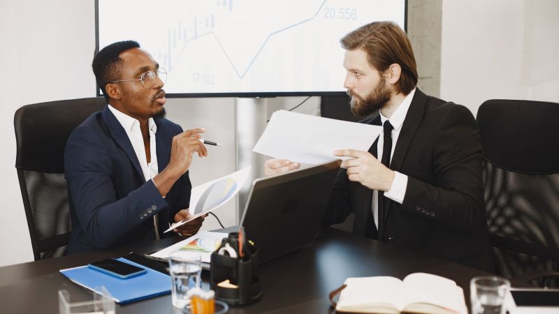 Two business professionals engaged in a planning meeting, discussing documents in a modern office setting. — Using MetaTrader