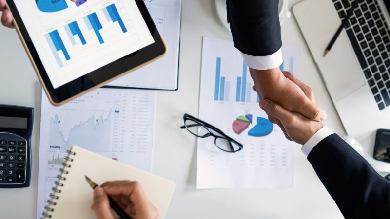 Business professionals handshake over graphs and charts in a corporate setting, symbolizing successful negotiation and agreem