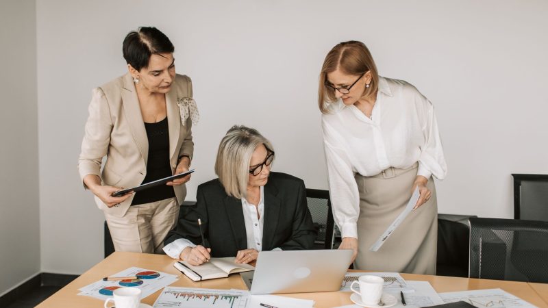 Three businesswomen discussing documents during a meeting in a modern office setting. — Your Perfect Blend: Ejuice Selections