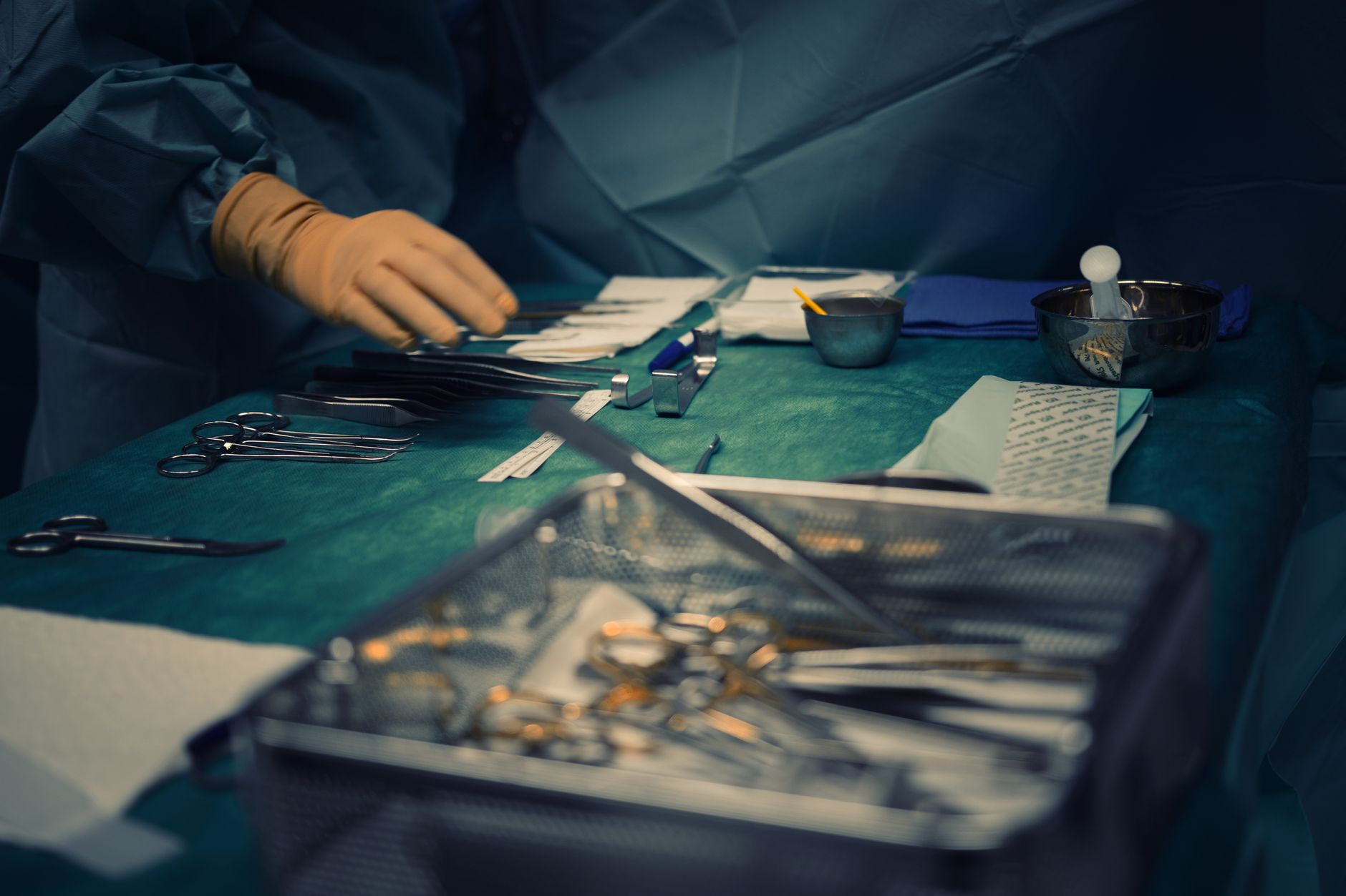 surgical instruments laid out on a green operating table with a gloved hand